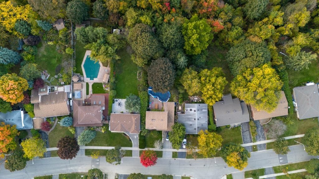 Aerial view of suburban neighborhood with houses, trees, and a swimming pool.