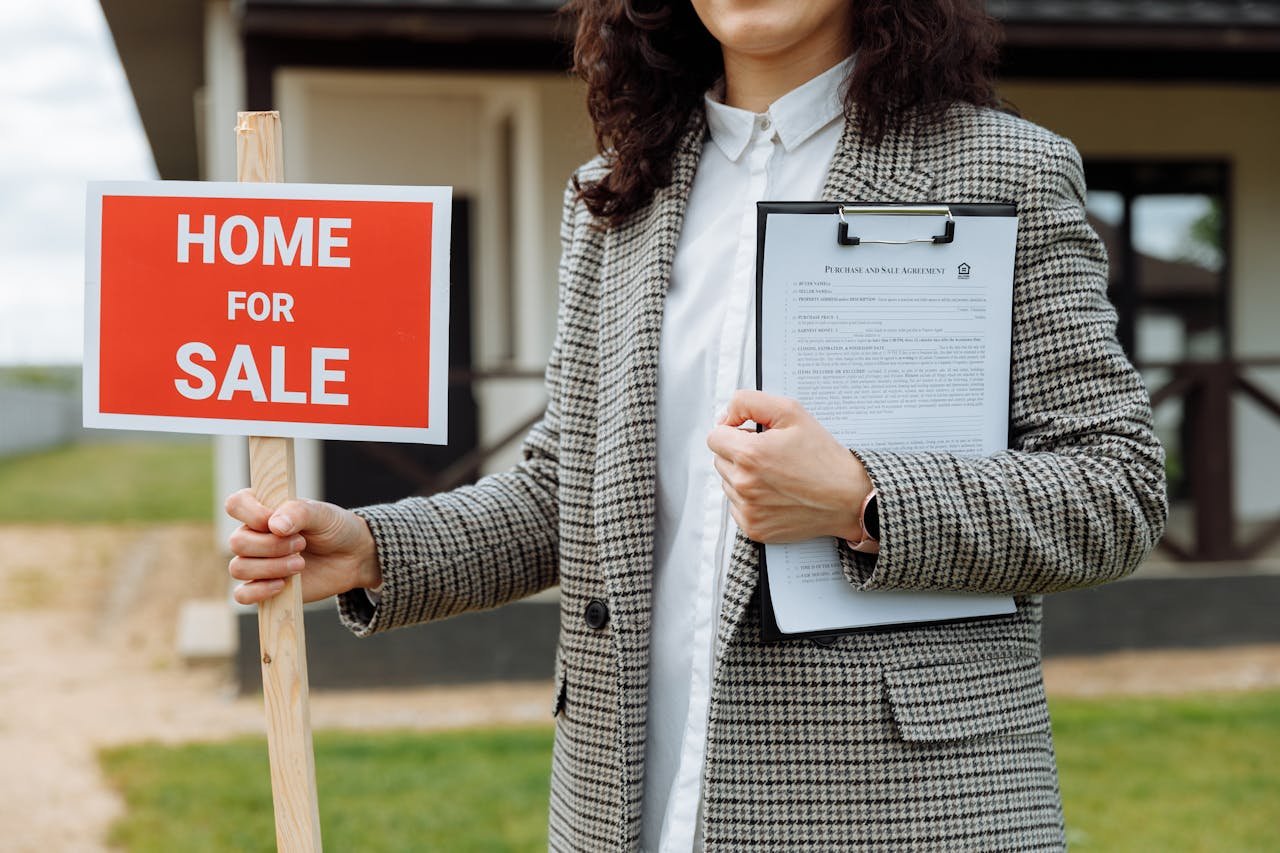 gallery-2 A real estate agent holding a home for sale sign and clipboard outside a property.