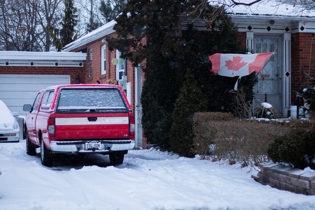 services-01 A red truck parked in a snowy Toronto front yard with a Canadian flag waving by the brick house.